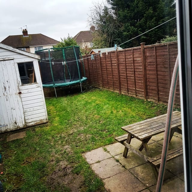 Photo of the garden: lawn, brown fence, white shed, washing line, picnic table